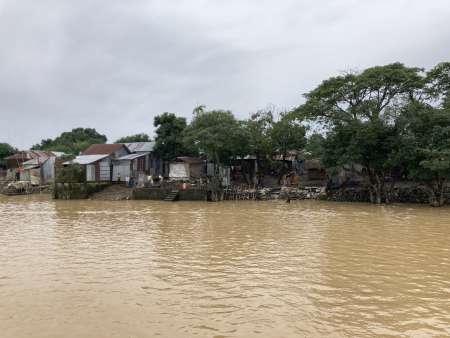 Flood-damaged and sandbag-reinforced shoreline of Bangladeshi village surrounded by muddy water