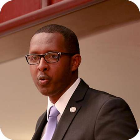 profile of dark-skinned man with glasses in suit with purple tie