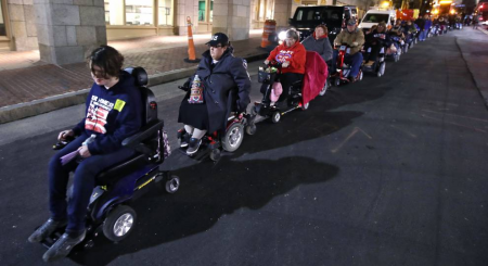 Disability rights activists convoy down Beacon Hill after being charged with trespassing at the McCormick Building, which houses the Massachusetts Executive Office of Health and Human Services, in Boston, on Nov. 1, 2016.Line of people using wheelchairs, 